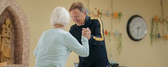 ein Mann mit Brille tanzt vorsichtig mit einer aelteren Bewohnerin
