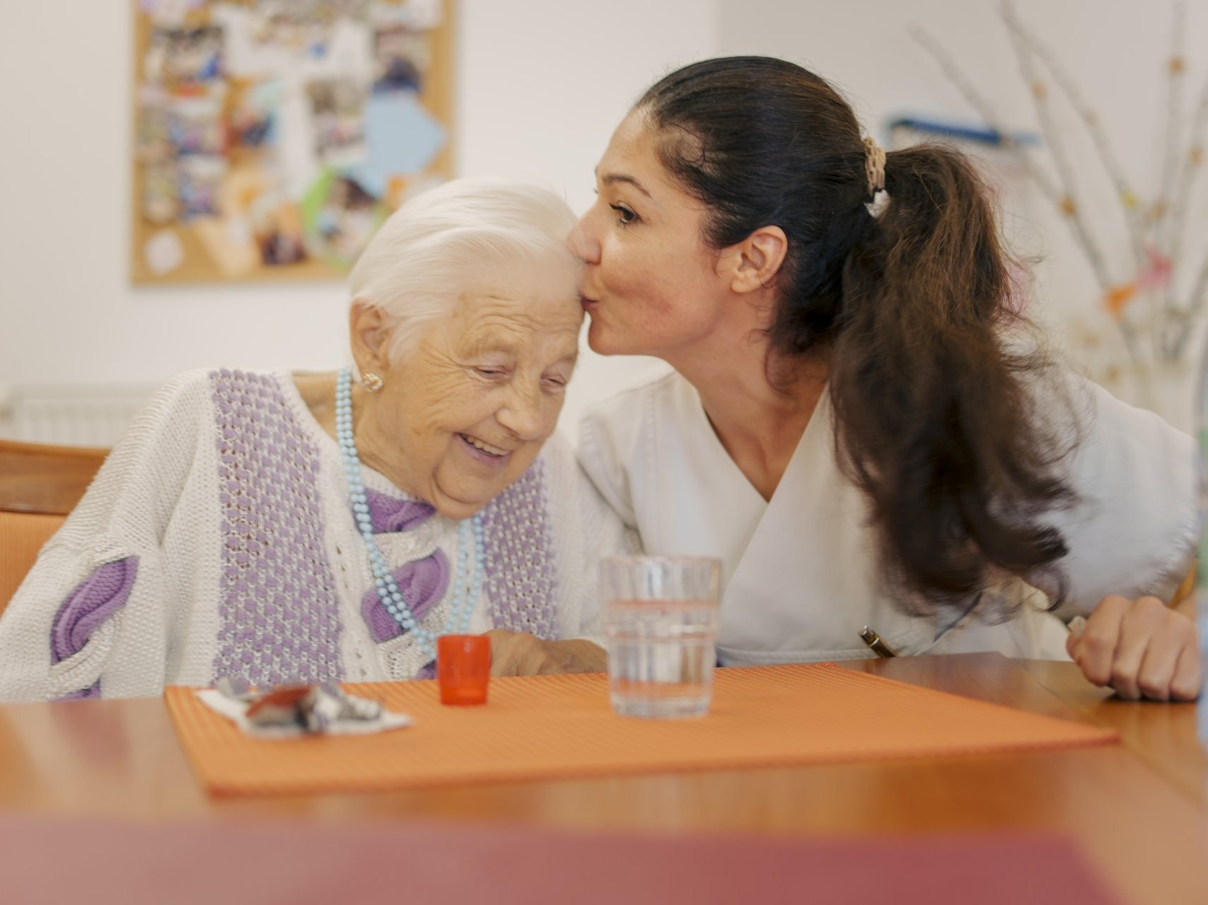 eine Pflegerin gibt einer Bewohnerin einem Kuss auf die Stirn